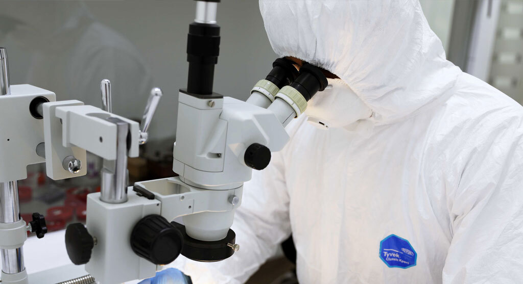 Techniker im Reinraumanzug untersucht eine Probe unter einem Mikroskop.