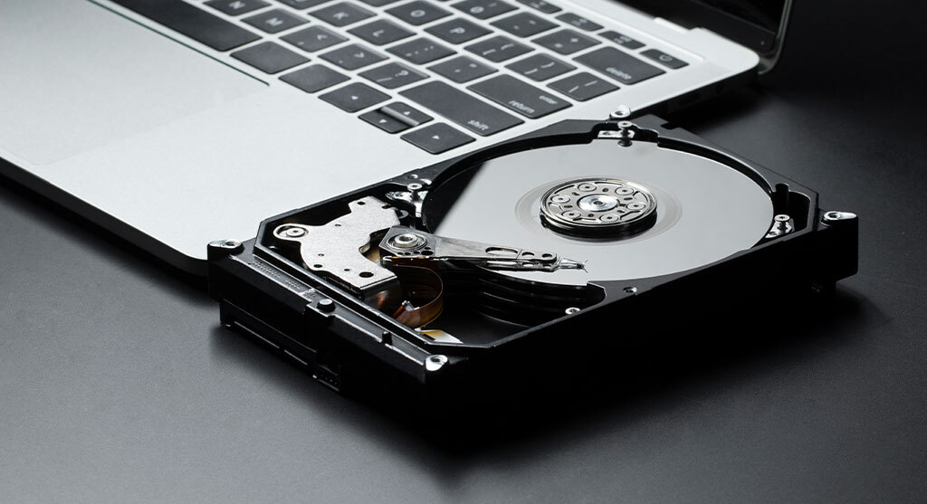 Geöffnete Festplatte neben einem Laptop auf dunkler Oberfläche.